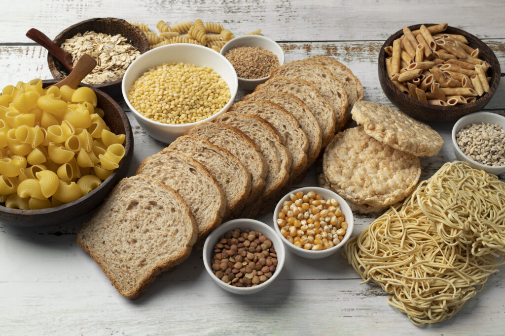 Variedad de alimentos ricos en carbohidratos como pan integral, quinoa, frutas y legumbres.